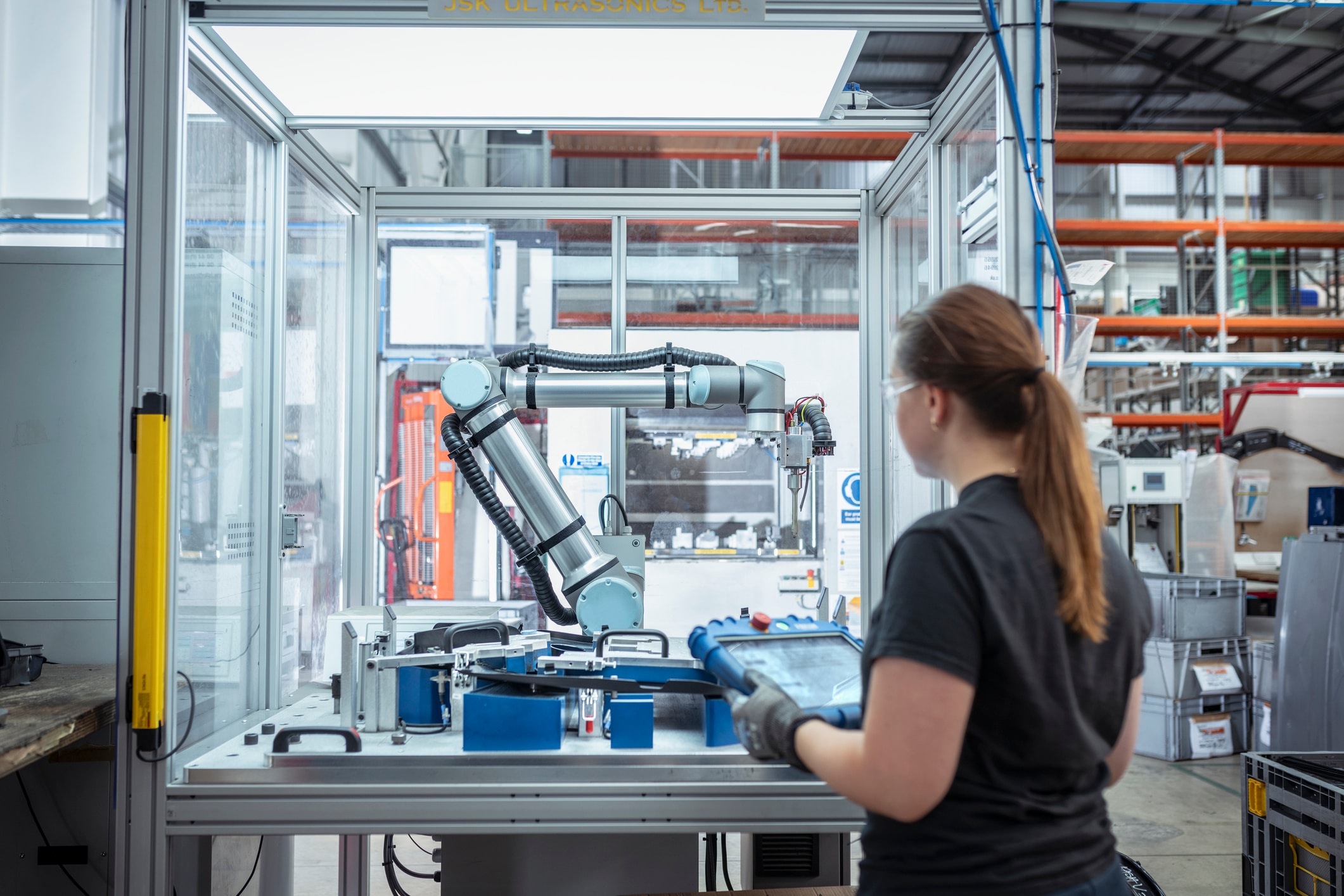 A worker in an automotive parts factory holds a tablet that she’s using to program and control a nearby robotic assembly machine.