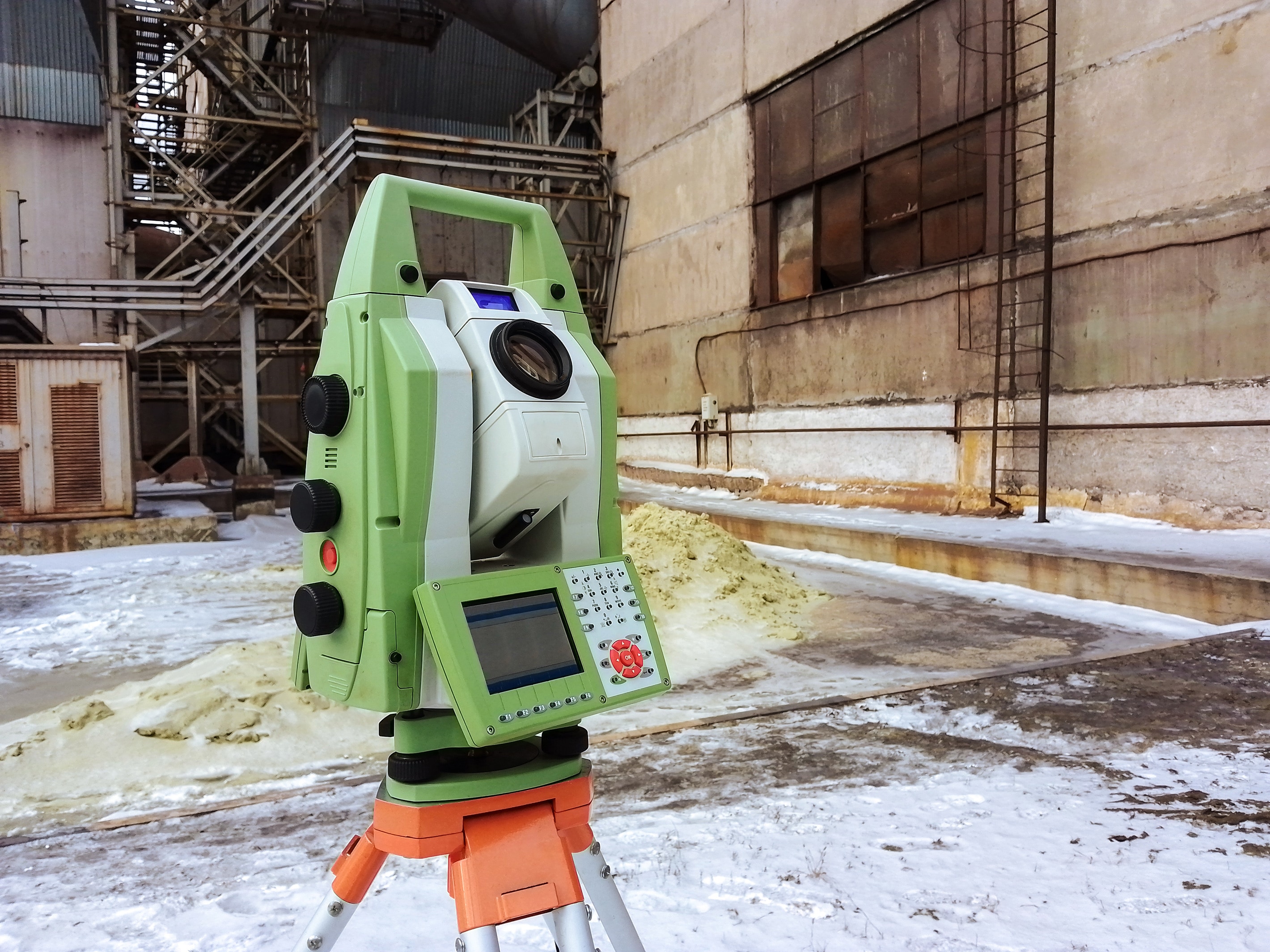 A 3D laser scanner is in front of an industrial building in the snow.
