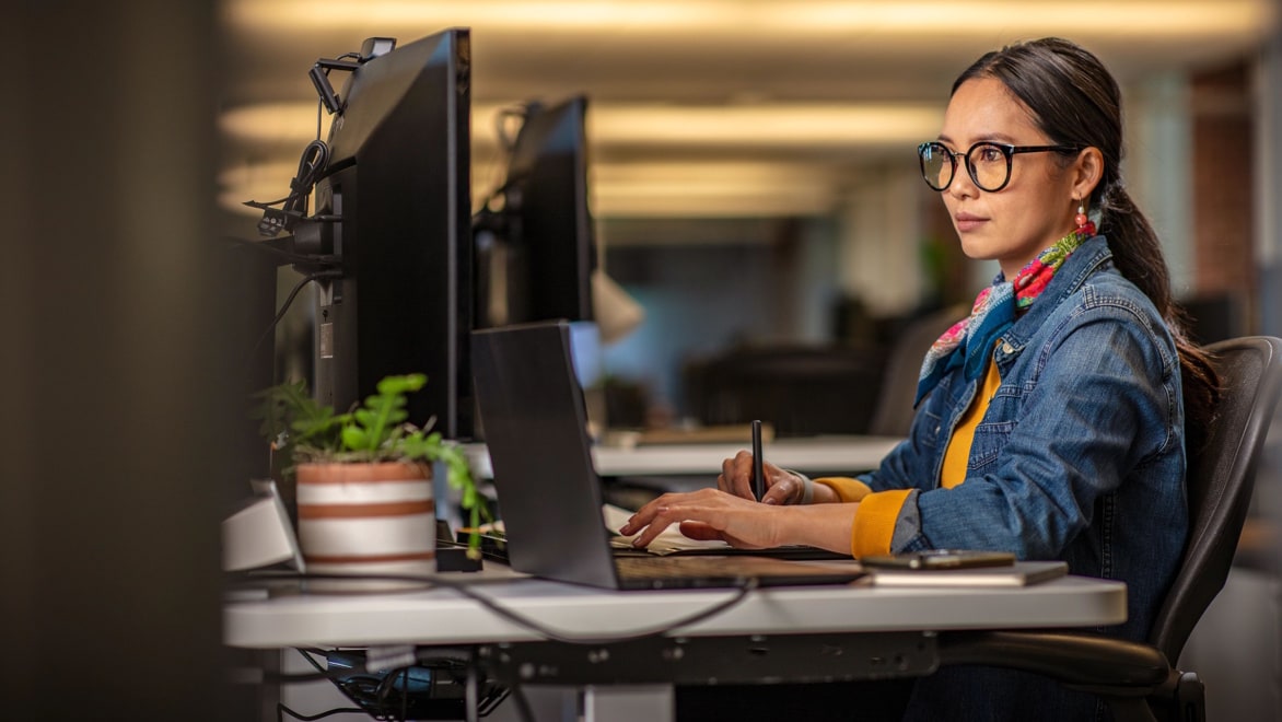 Person working at a desk, using a laptop and dual monitors while reviewing data protection and privacy information in a modern office.