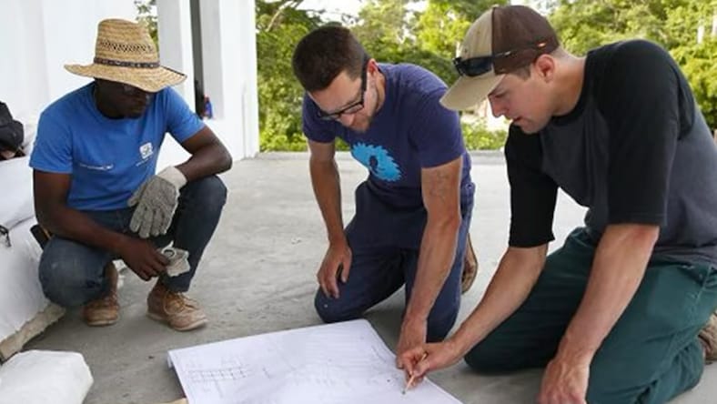 Three BHI employees looking at blueprints that are laid out on the concrete ground at a BHI project site.