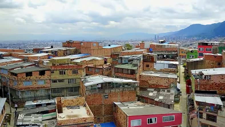 Aerial view of area with densely populated buildings in Bogotá, Colombia, on a cloudy day. Mountains in the background on the right side of the frame.