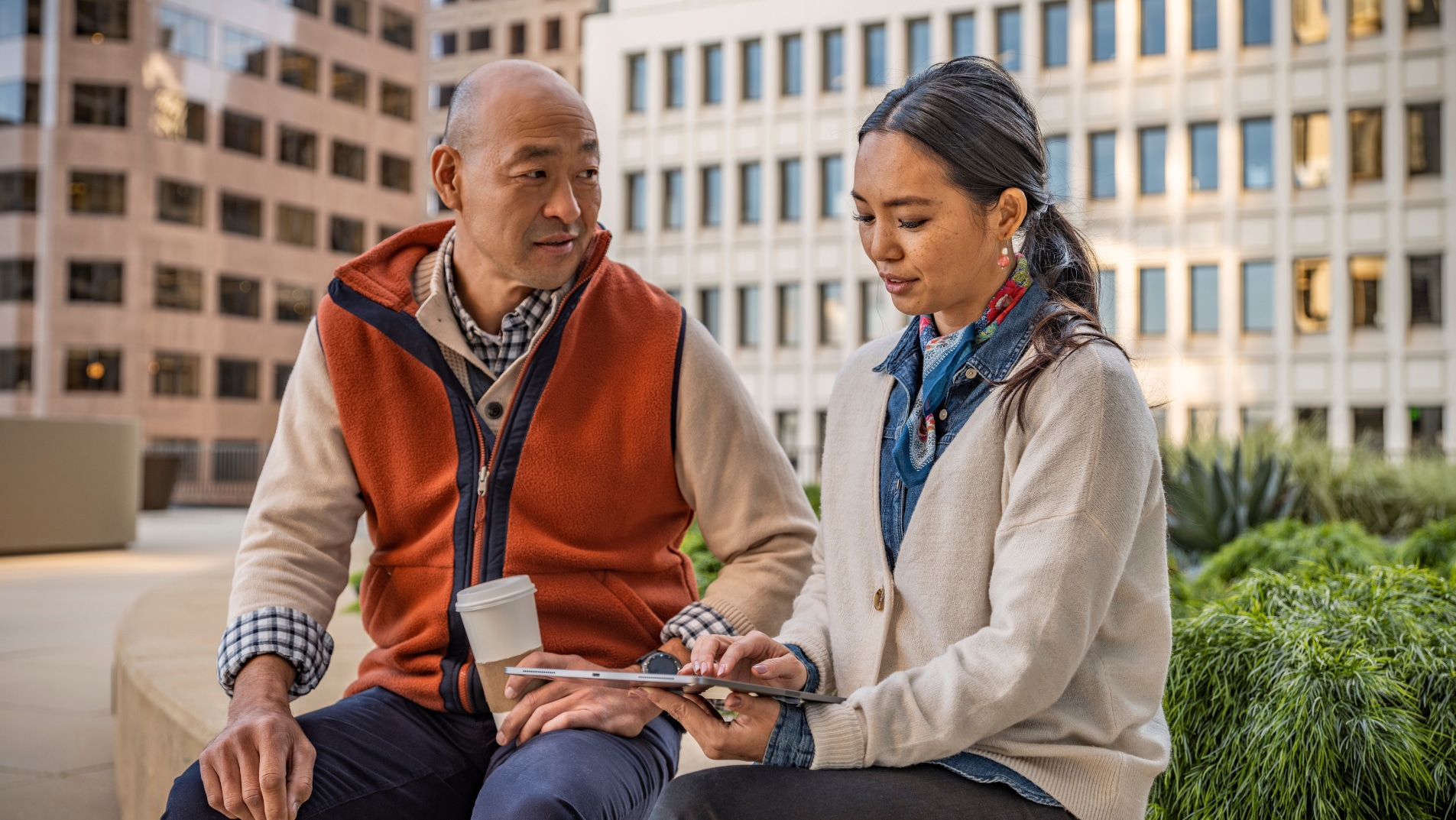 Two employees review information on a tablet while seated in an outdoor workspace.