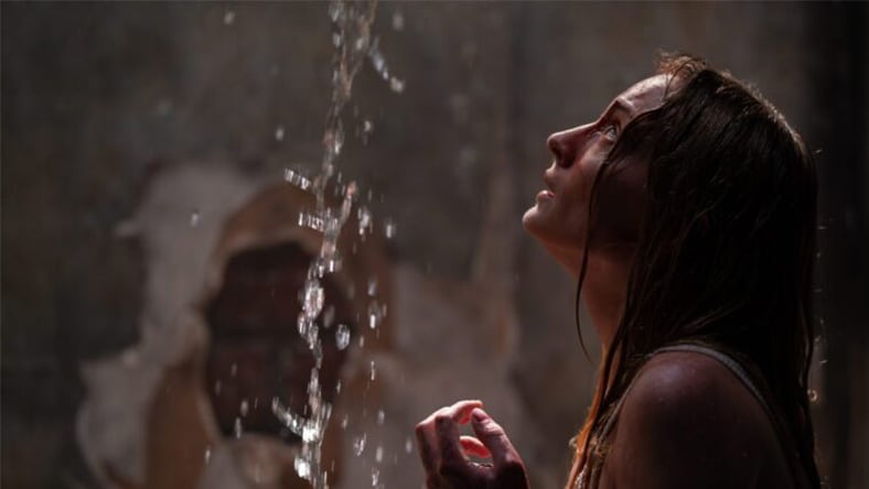 A person standing under a stream of water with a textured wall in the background.
