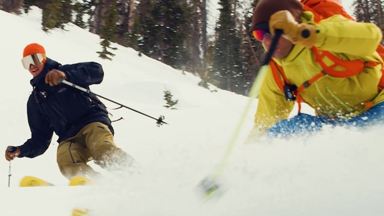 Low-angle shot of 2 men downhill skiing.