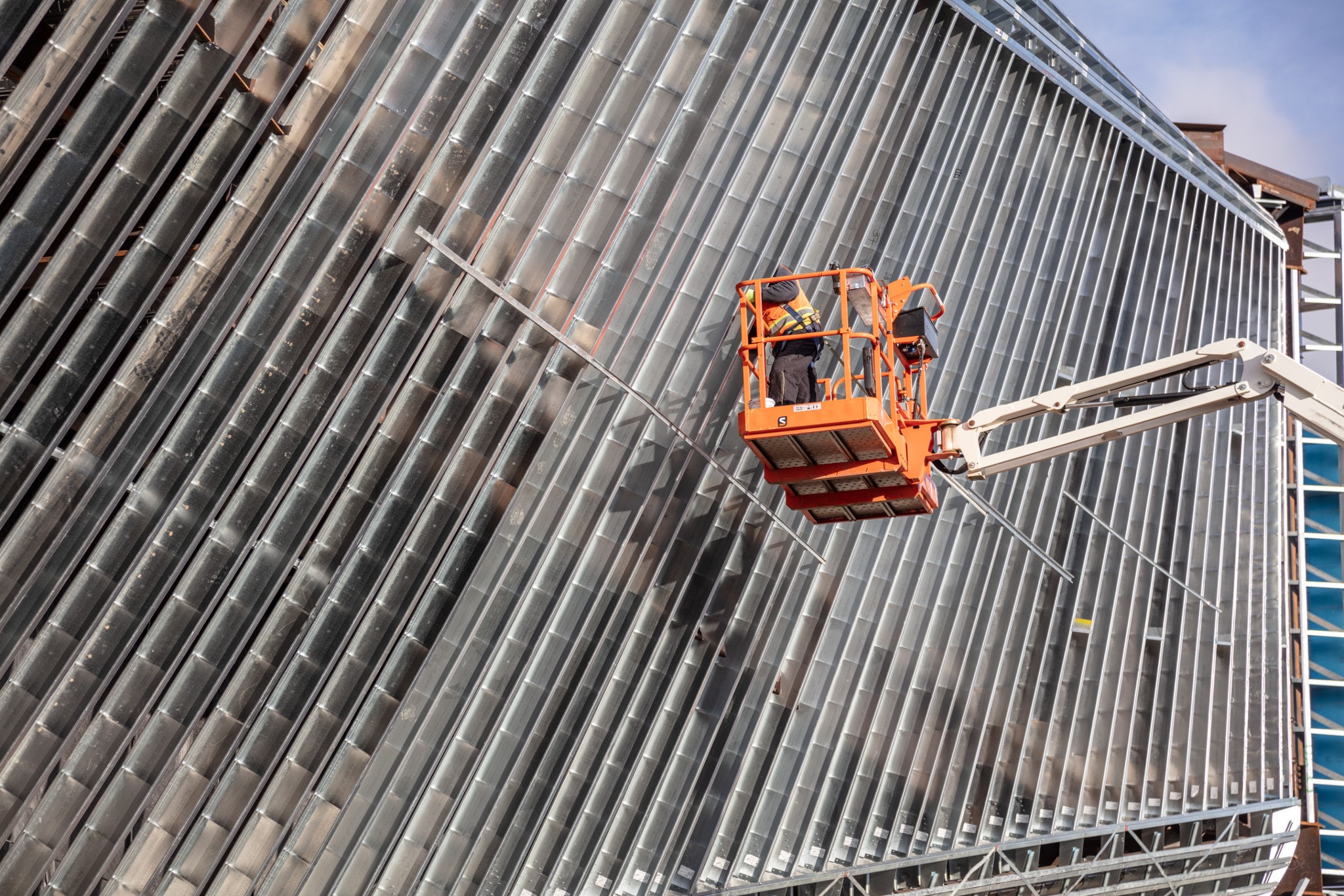 Construction worker in a safety lift working on the exterior of a modern ribbed metal building.