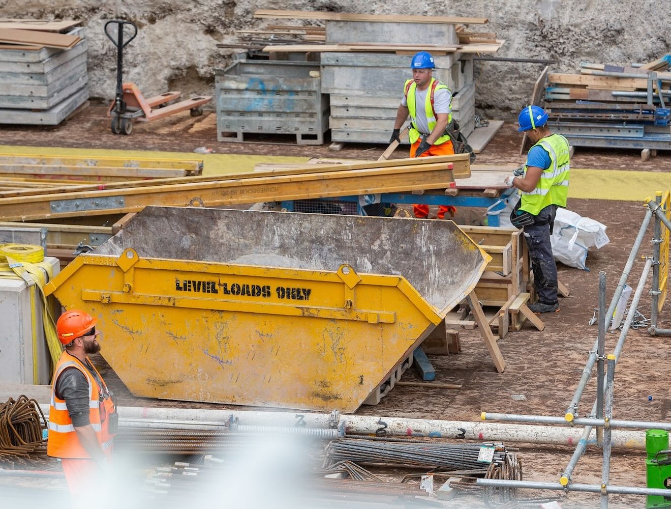 At a construction site, a dumpster is surrounded by workers in hard hats.