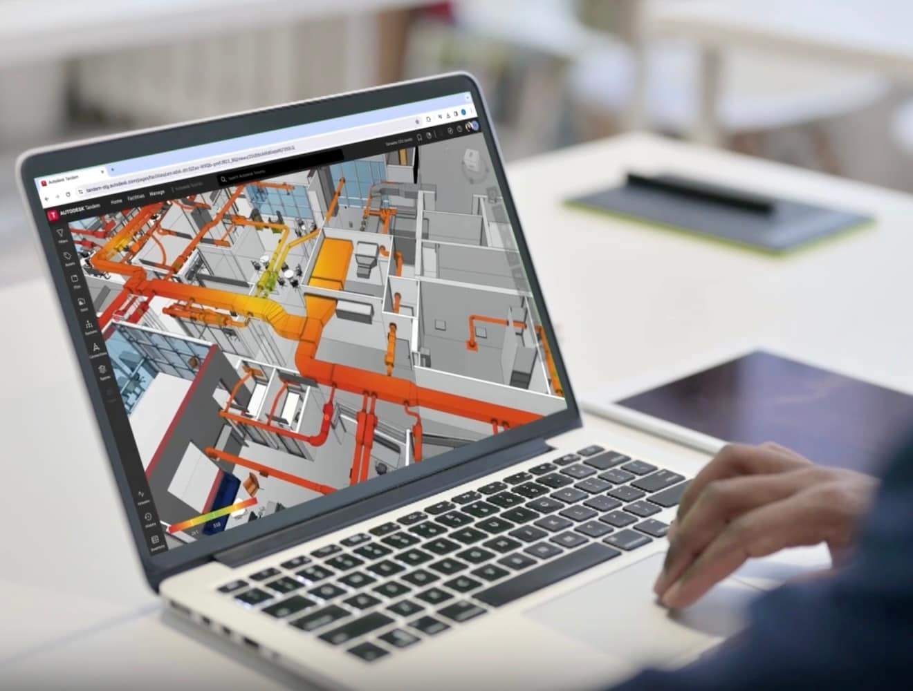 A person works on a laptop computer that displays a screen of a digital twin within Autodesk Tandem software.