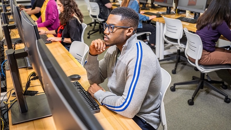 A young man works on a computer in a college classroom