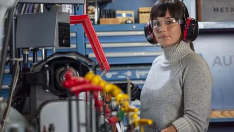 female engineer with safety goggles and hearing protection working behind a machine