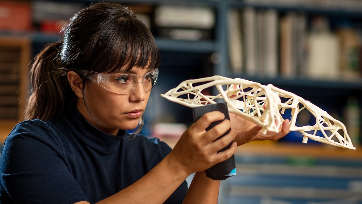 A woman examines an intricate 3D-printed plastic object.