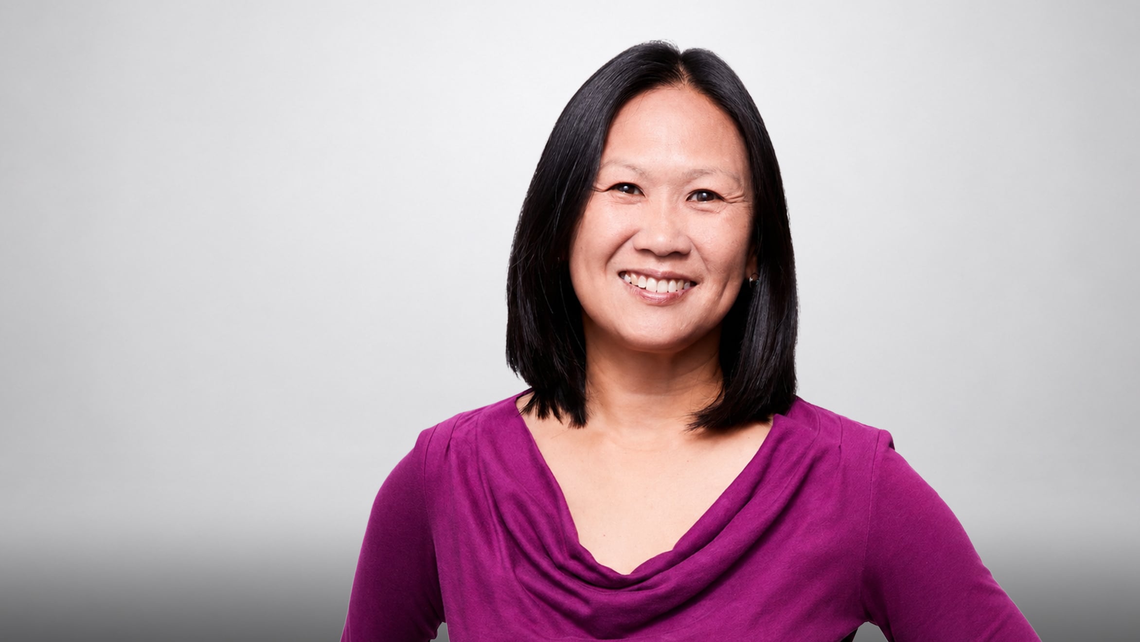 Smiling person with short hair wearing a purple top against a light background.