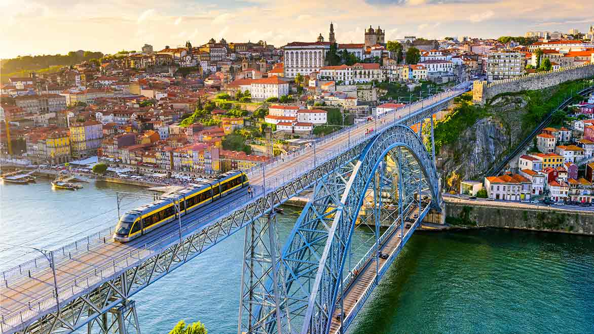 Light rail train crossing a bridge with a city in the background