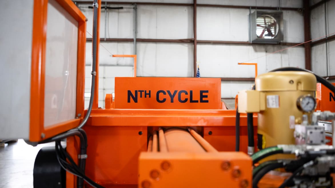 Side view of Nth Cycle "OYSTER" electro-extraction machine. The machine is highlighter orange with a prominent "Nth Cycle" logo, located in a large warehouse space.