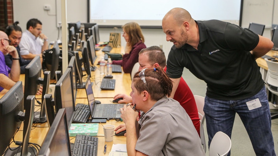 An instructor assists an adult student working on a laptop.