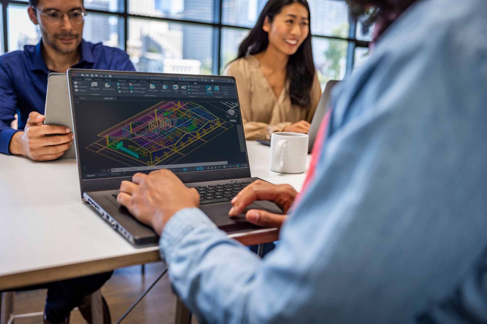 User working in AutoCAD on a laptop displaying a detailed building model while collaborating with team members at a table.
