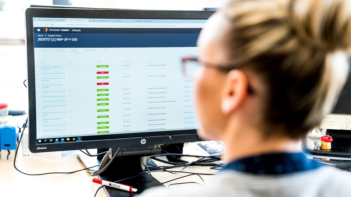 Over-the-shoulder view of a woman working on a computer displaying manufacturing production software.