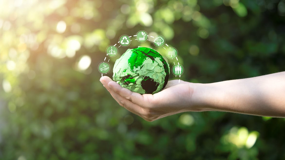 Person holding green scrap paper ball with world map and environment icon.