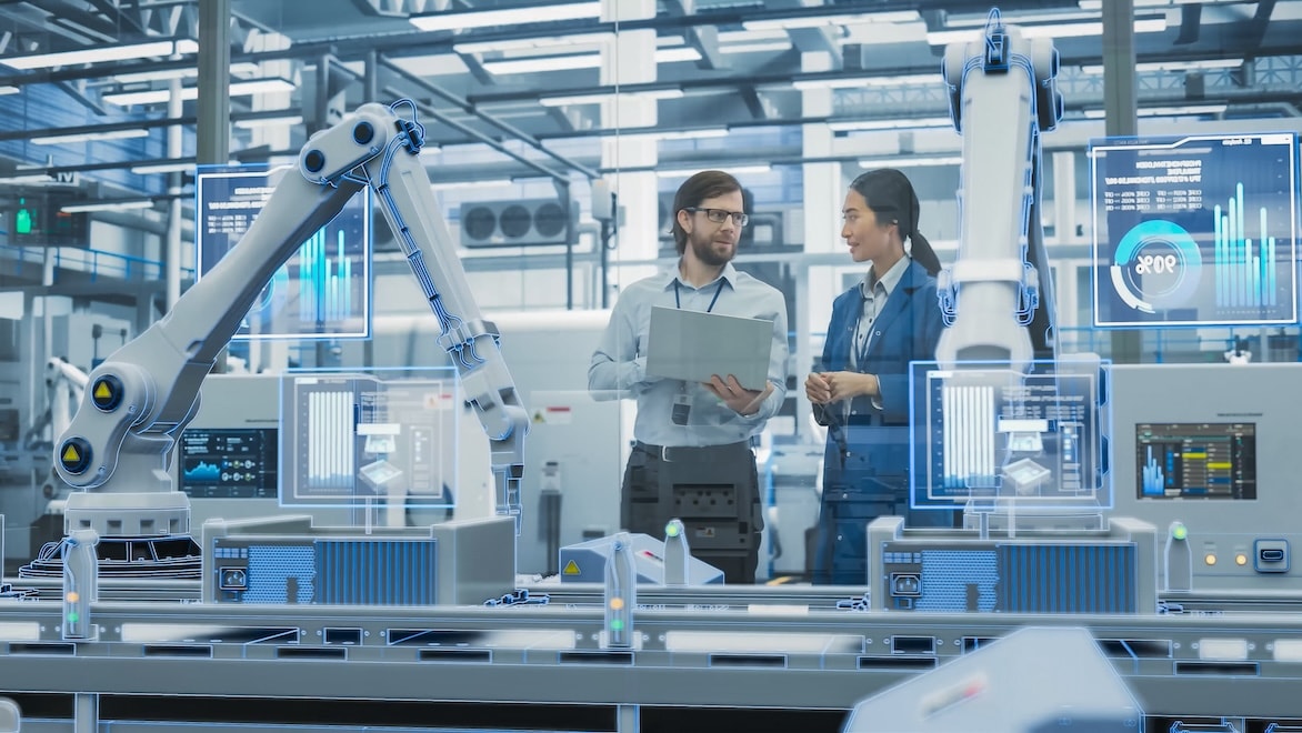 2143499707 Two factory managers discuss operations in front of an automated production line with robot arms and a graphic overlay representing continuous data collection and reporting.