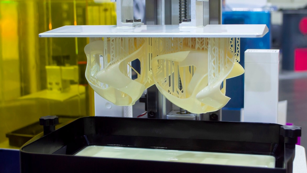 Close-up of a stereolithography printer showing a printed object suspended over liquid photopolymer resin.