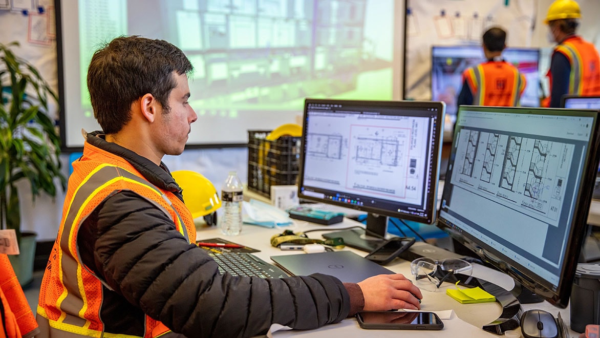 Construction professional reviewing digital plans on computer screens.