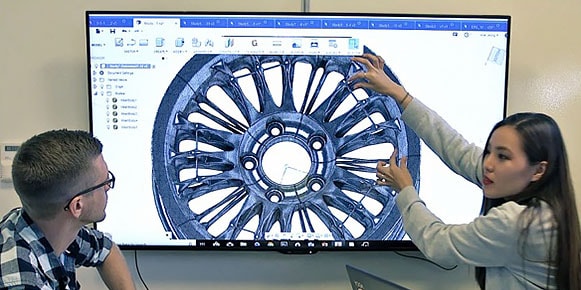 Hombre y mujer mirando el diseño de una rueda en una pantalla grande