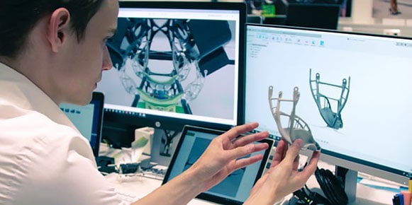 画面に設計が映る部品と同じ部品を持ち上げる男性