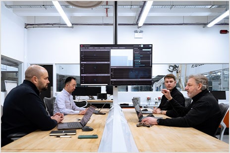 Four team members collaborate in front of a screen displaying operational data.