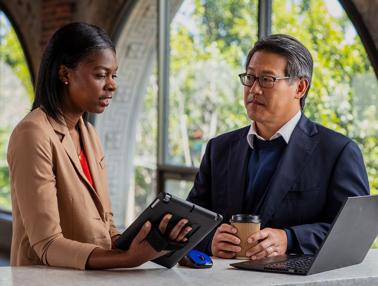 Two professionals reviewing data on a tablet beside a laptop in an office.