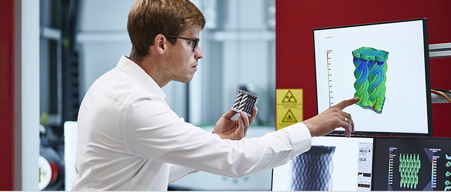 A man working in a technology center holding a product model in one hand while comparing it to a digital model on the computer screen. 