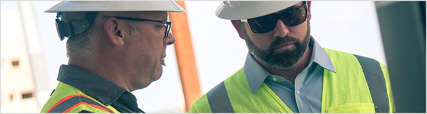 Dos hombres en un emplazamiento de construcción ven dibujos en una tableta mediante la aplicación AutoCAD móvil. 