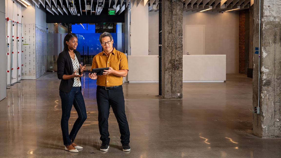 Two people standing in an industrial space; one is holding a tablet 