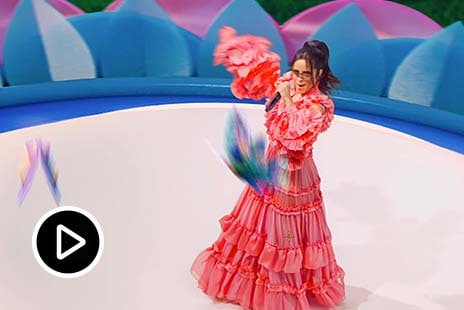 Video: collage di Camila Cabello che canta e balla in abito elegante su un palco davanti ad uno schermo verde 