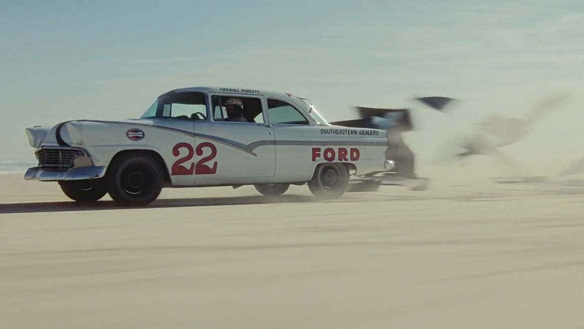 Driver in a white Ford with a red 22 painted on its side speeds through sand on beach in a scene finished with Autodesk Flame 