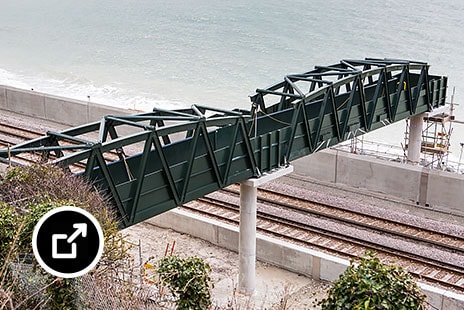 A fibreglass footbridge over railroad tracks by the sea