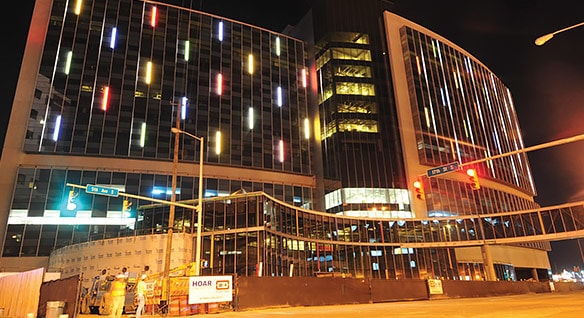 Nighttime view of new 12-floor children’s hospital building with a front of dark glass lit up by multi-colored panels