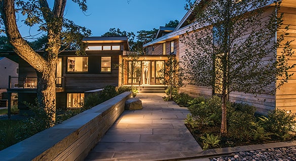 View at night of a walkway leading to a residential home surrounded by trees 