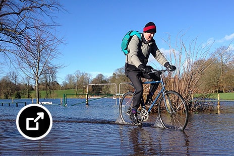 Person riding a bicycle through a flooded park