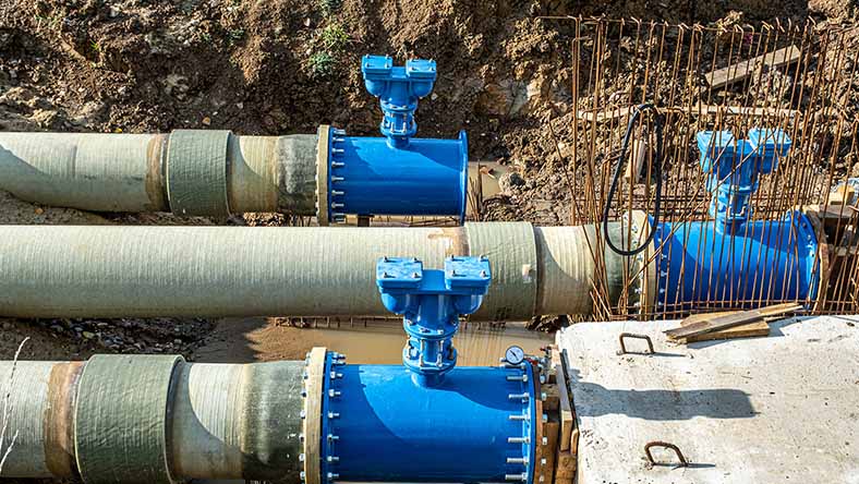Large industrial water pipes installed in a trench, surrounded by excavated earth and construction materials
