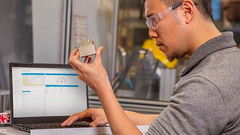 Image showing a worker inspecting part quality using Autodesk Fusion Operations and Quality Analytics reports.