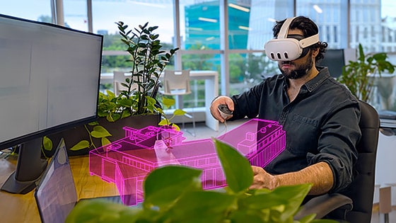 Man at desk in VR headset pointing to virtual building graphic overlay