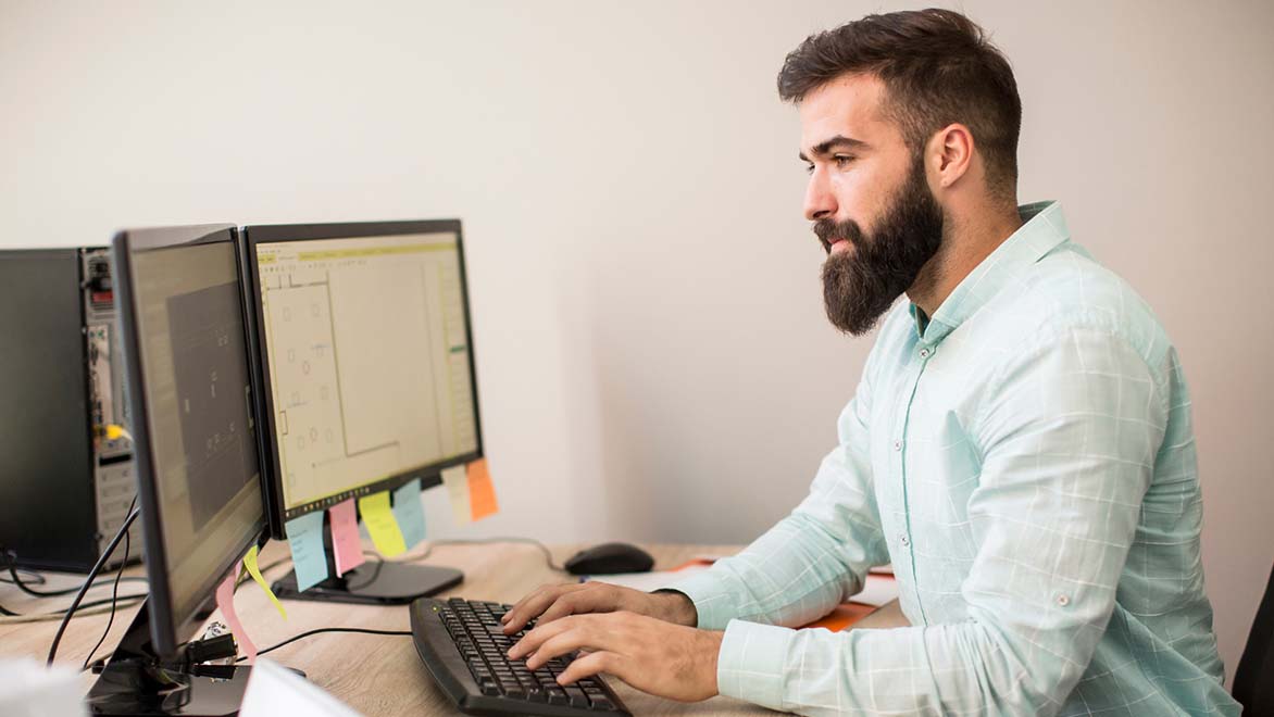 En man som tittar på en materialförteckning på två datorskärmar 