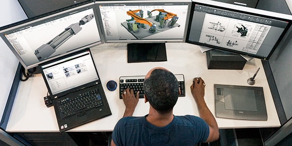 Ingeniero mecánico usa dibujos CAD en varias pantallas