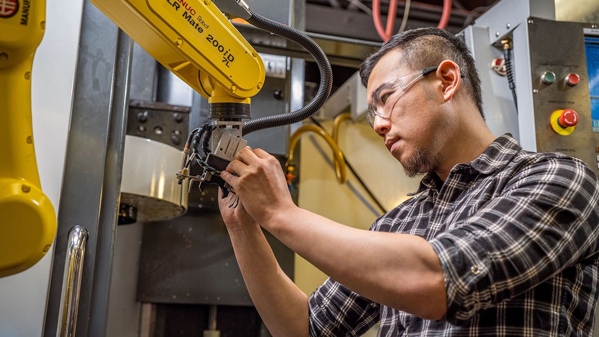 Man adjusting a tool on the end of a robotic arm in a CNC lab
