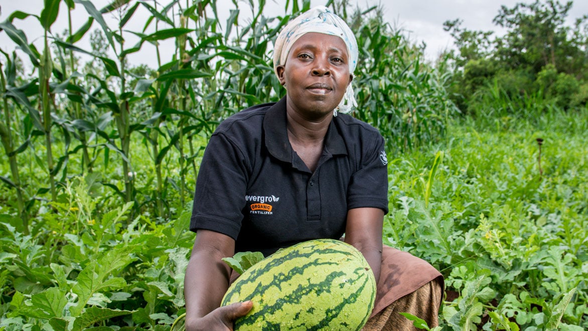 Woman in a black shirt poses with a watermelon in a field in Kenya