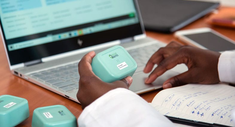 Person holds small blue Nexleaf device in front of a computer