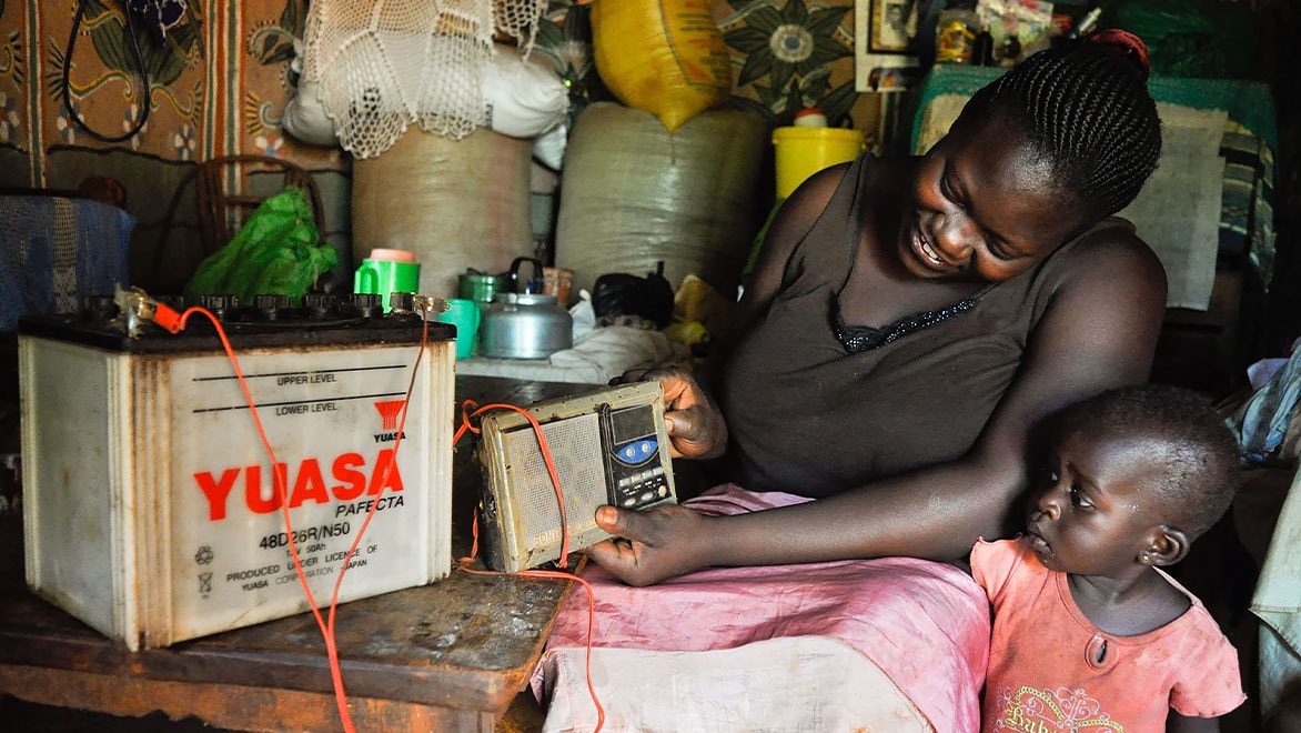 A woman and her young child looking at a radio powered by a large battery