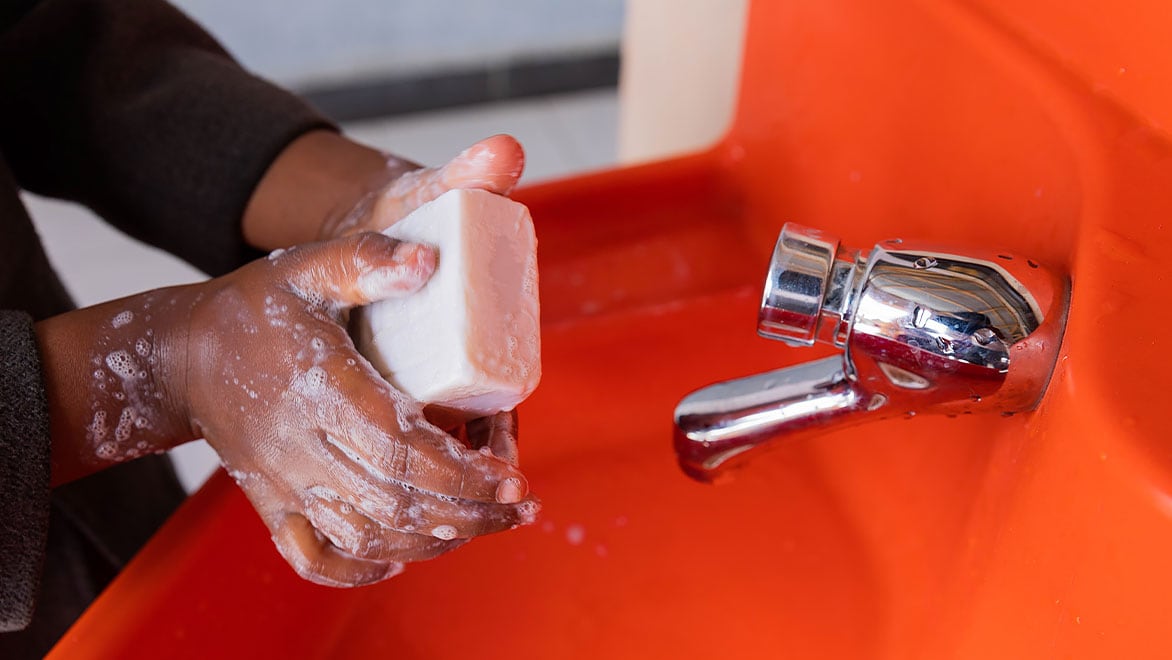Two hands holding a bar of soap, lathering and washing at an orange-colored Splash handwashing station.