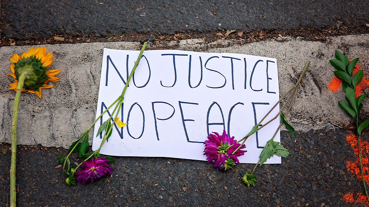 Close-up of sign saying “No justice no peace” surrounded by flowers    