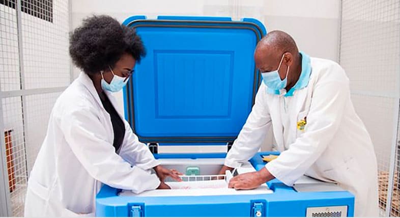 Man and a woman in white lab coats stand over a blue vaccine container
